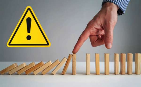 consequence - Municipal Debt Specialist Yellow warning triangle with exclamation mark; a hand stops a row of wooden dominoes from falling.